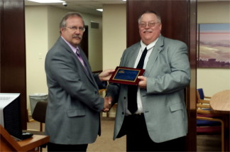 Riley County Emergency Management Director Pat Collins, right, receives the 2015 KEMA Professional of the Year Award from Geary County Emergency Management Director Garry Berges during Monday morning's Riley County Commission meeting. (Staff photo by Brady Bauman)