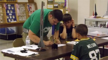 INSPECTION: Tony Foster, left, looks over a model rocket constructed by apparent Jordy Nelson fan Easton Breault, sitting right, of the Randolph Ramblers 4-H Club. Foster said interest in rockets and space in general has grown among 4-Hers. (Staff photo by Brady Bauman.)
