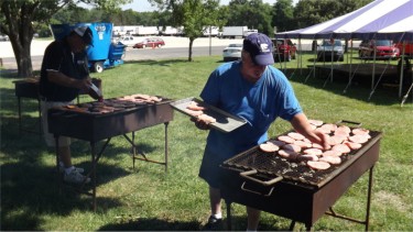 HEAT IS ON: Blue Valley Pork Producers members Larry Hoobler, left, and Jim Feldkamp prepare pork burgers Friday afternoon at the Riley County Fairground. The pork burgers were served later that evening during the Riley County Fair. (Staff photo by Brady Bauman)