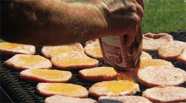 TIS THE SEASON: A member of the Blue Valley Pork Producers seasons pork burgers on an open grill Friday afternoon at the Riley County Fairground. Friday night was the annual Blue Valley Pork Producers pork burger feed at the Riley County Fair. (Staff photo by Brady Bauman)