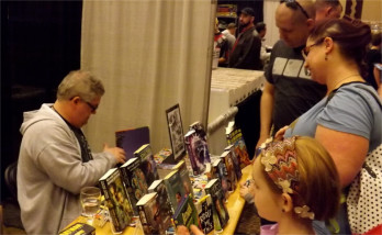 Novelist and senior writer at Hallmark Cards in Kansas City, Mo., Kevin Dilmore, readies a book for a family at the Little Apple Comic Con Saturday.