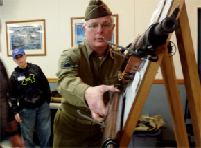 Dave Hurska of the World War II Historcial Reenactment Society reaches for a WWII-era rifle Saturday inside the Manhattan American Legion. 