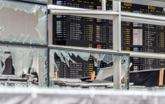 An arrivals and departure board is seen behind blown out windows at Zaventem Airport in Brussels on Wednesday, March 23, 2016. Belgian authorities were searching Wednesday for a top suspect in the country's deadliest attacks in decades, as the European Union's capital awoke under guard and with limited public transport after scores were killed and injured in bombings on the Brussels airport and a subway station. (AP Photo/Geert Vanden Wijngaert, Pool)